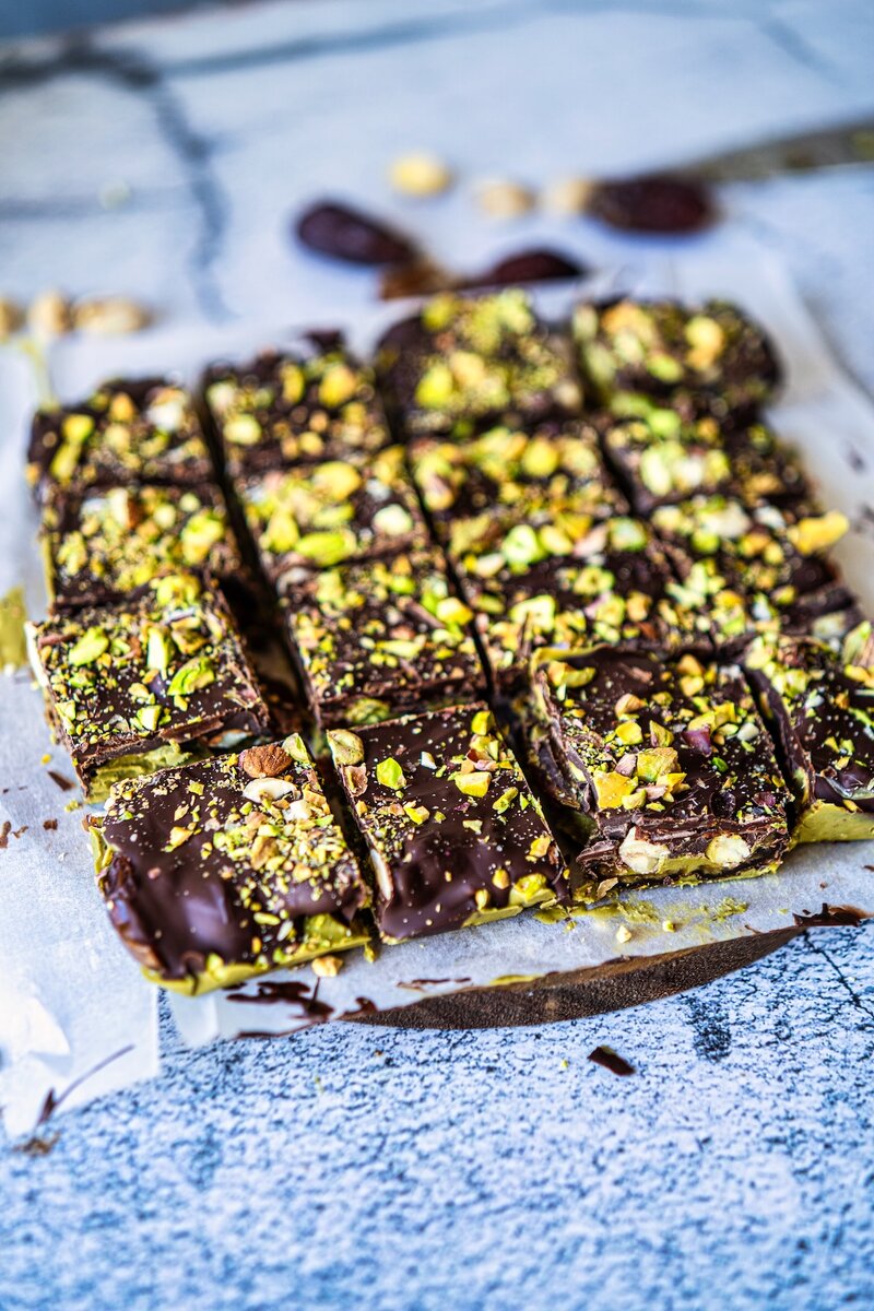 Image of No bake chocolate pistachio date bars cut into squares topped with chopped pistachios and dark chocolate