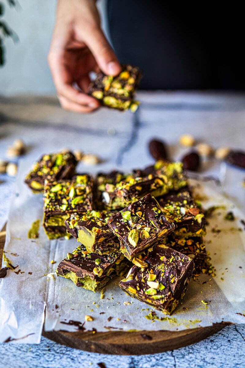 Hand holding a piece of no bake chocolate pistachio date bars showing texture and layers