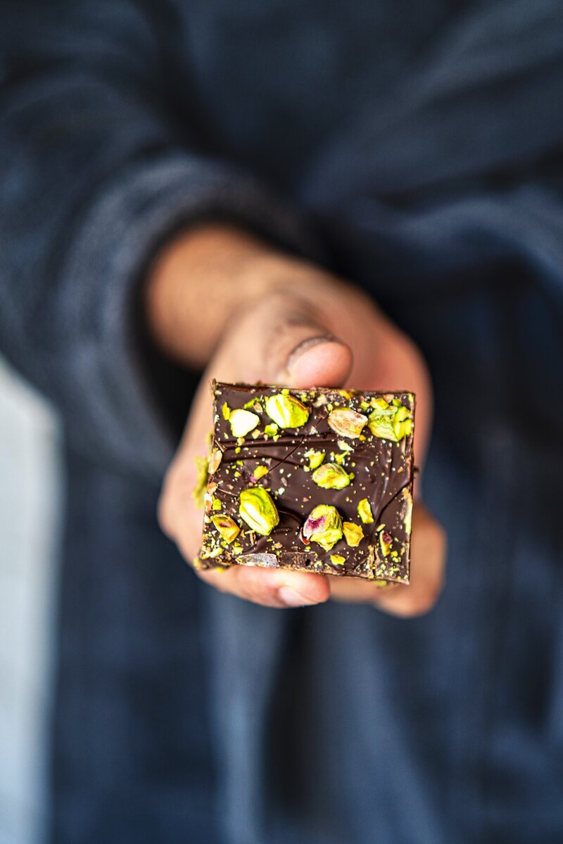 Close up of chocolate pistachio date bars topped with pistachios and smooth dark chocolate layer