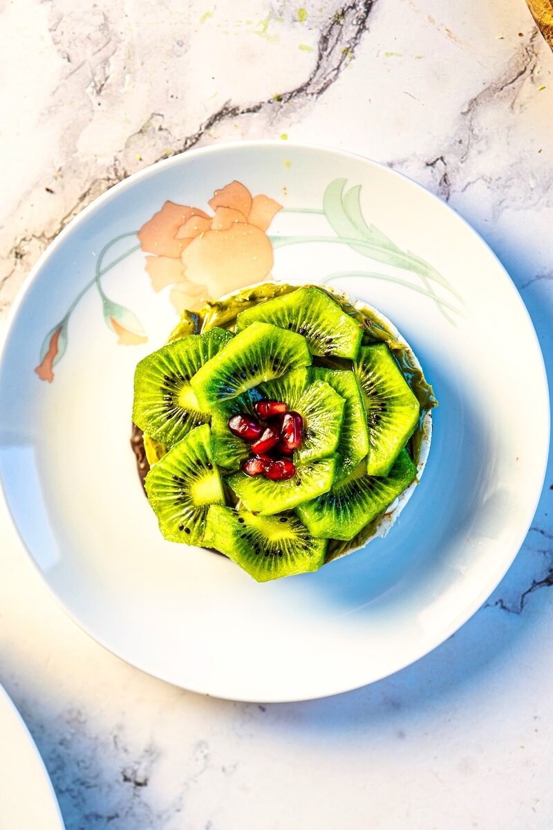 Hand holding a layered chocolate pistachio rice cake topped with fresh kiwi slices and pomegranate, healthy no bake dessert snack