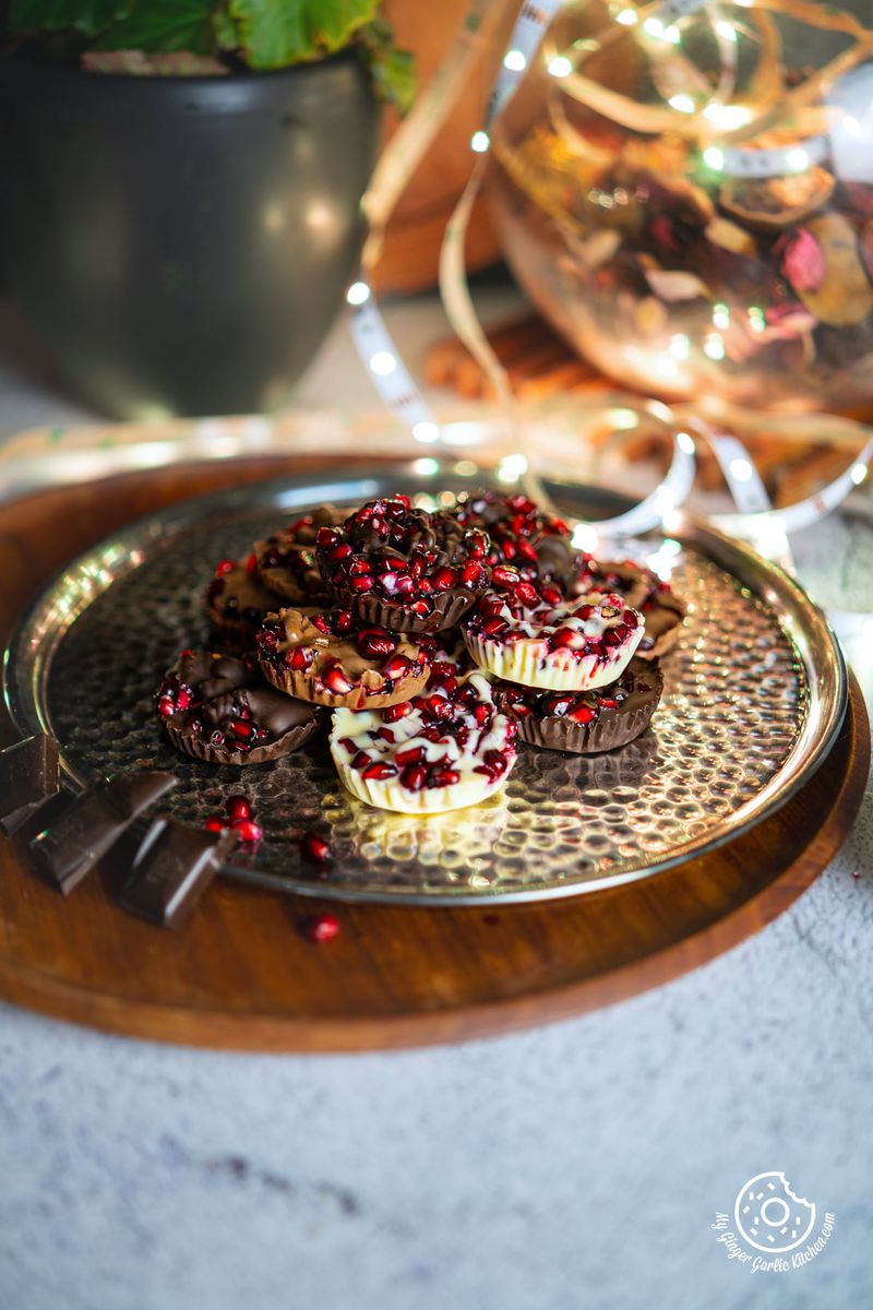 chocolate pomegranate bites in a stack on a metal plate with 2-3 chocolate pieces on the side