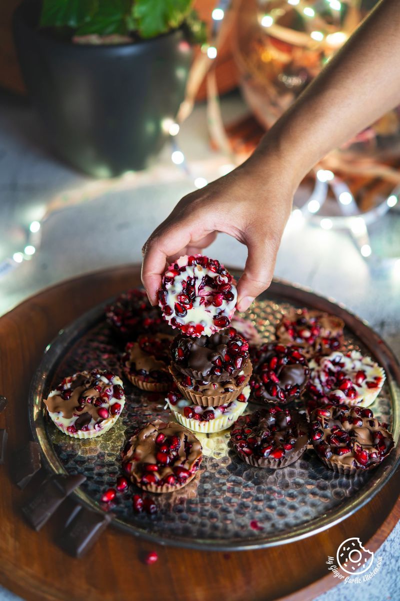 a hand holding white chocolate pomegranate bite over a metal plate with some more chocolate pomegranate bites