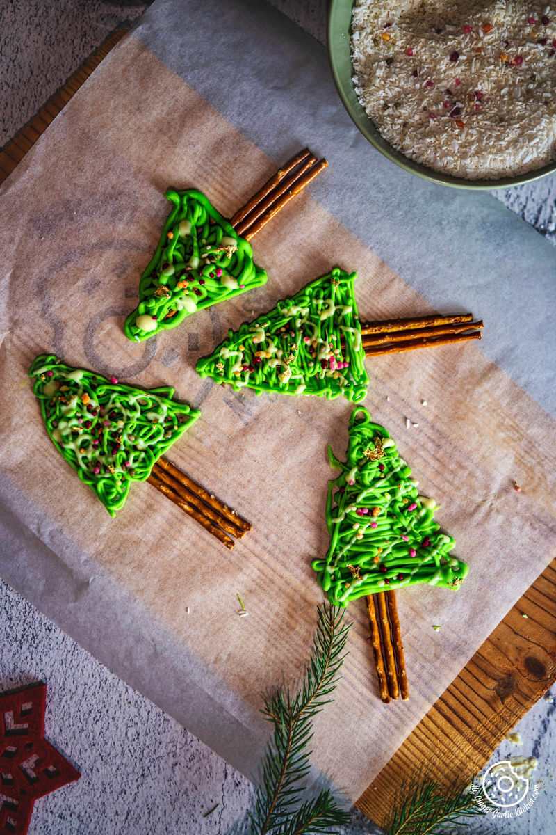 Overhead picture of four chocolate-covered pretzel Christmas trees on a piece of parchment paper.