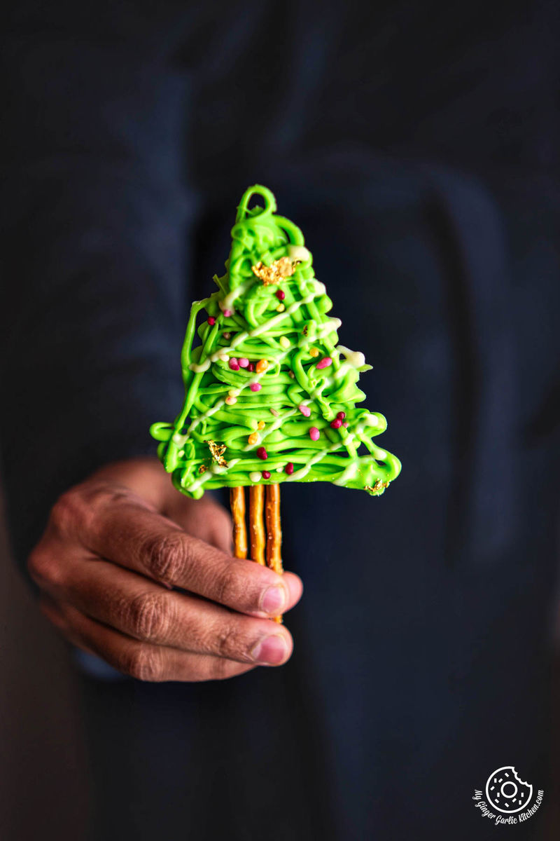 A hand holding a bowl of chocolate-covered pretzel sticks arranged in the shape of a Christmas tree.