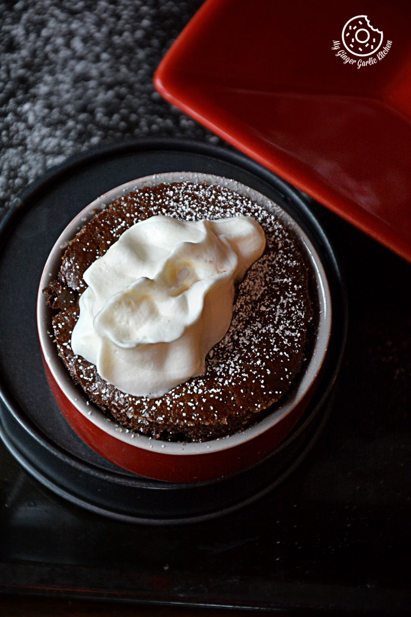 a small red bowl with a chocolate souffle and whipped cream on it