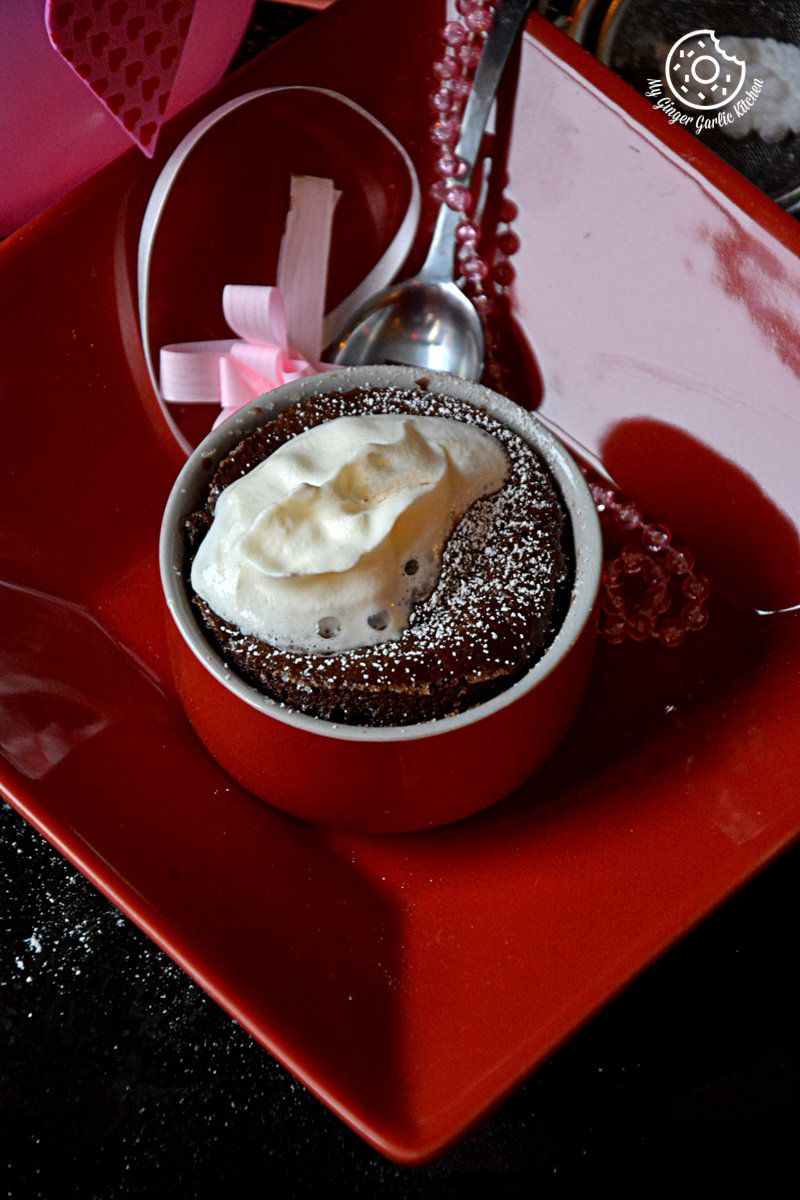 a red plate with a cup of chocolate souffle and a spoon