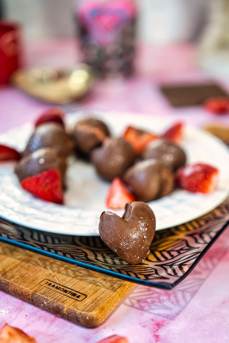 Close-up of a plate with chocolate-covered strawberry hearts and fresh sliced strawberries, set on a decorative surface