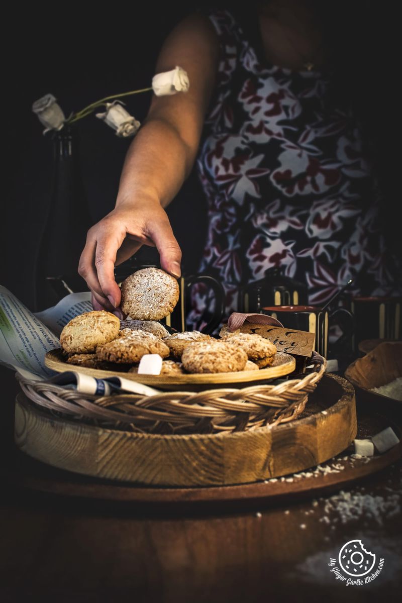 a hand is picking coconut cookie from the plate