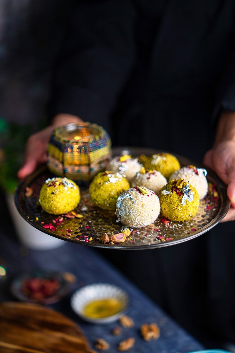 Festive coconut ladoo truffles served on a decorative plate, with creamy white chocolate pistachio filling tucked inside each sweet.