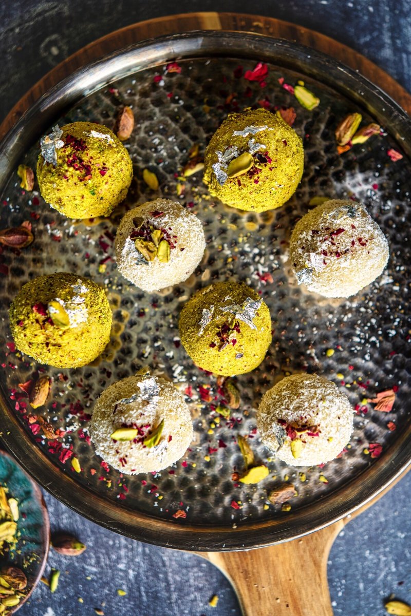 Coconut ladoo truffles coated in pistachio powder and desiccated coconut, garnished with pistachios, rose petals, and edible silver leaf.