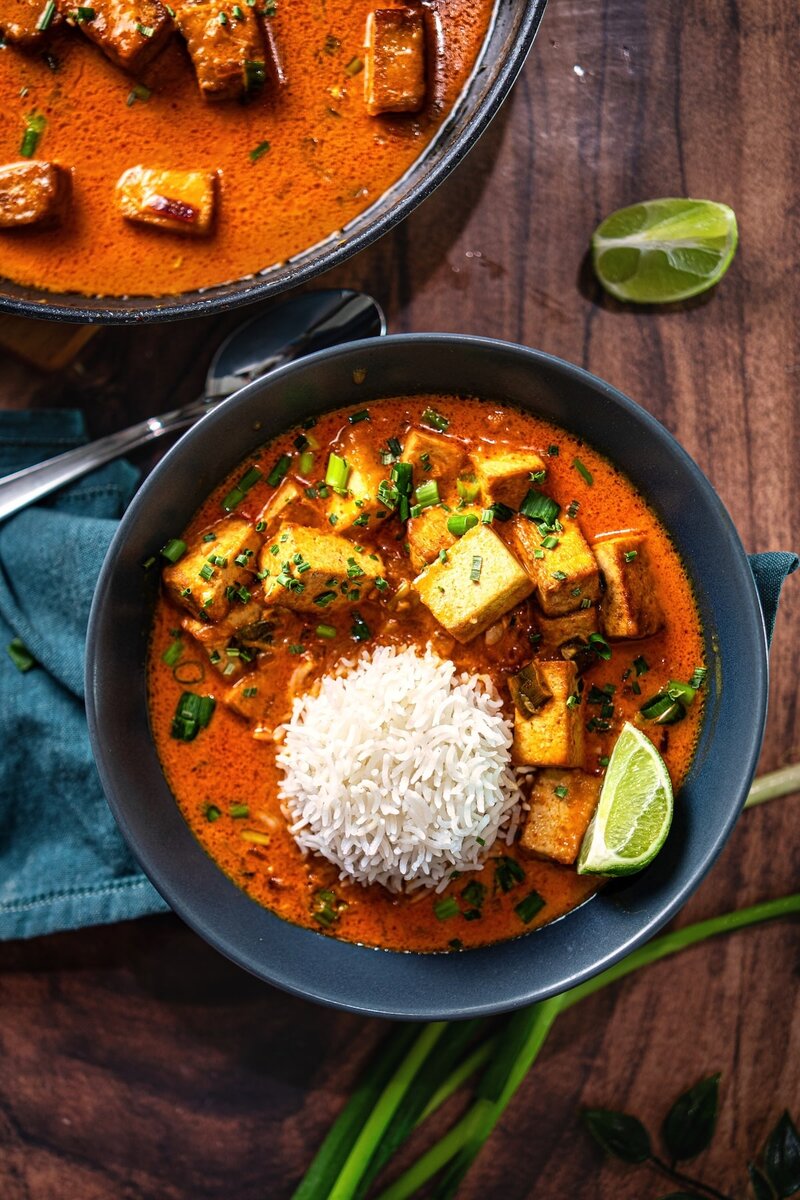 Top view of coconut lime tofu curry with rice and pan in background, rich creamy coconut sauce with pan-seared tofu