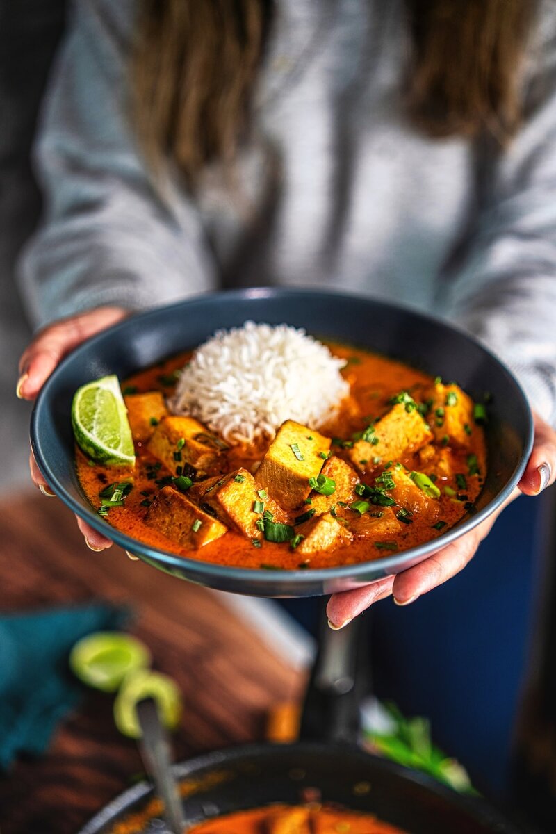 Serving coconut lime tofu curry in a bowl with rice, vibrant vegan curry garnished with herbs and lime wedge