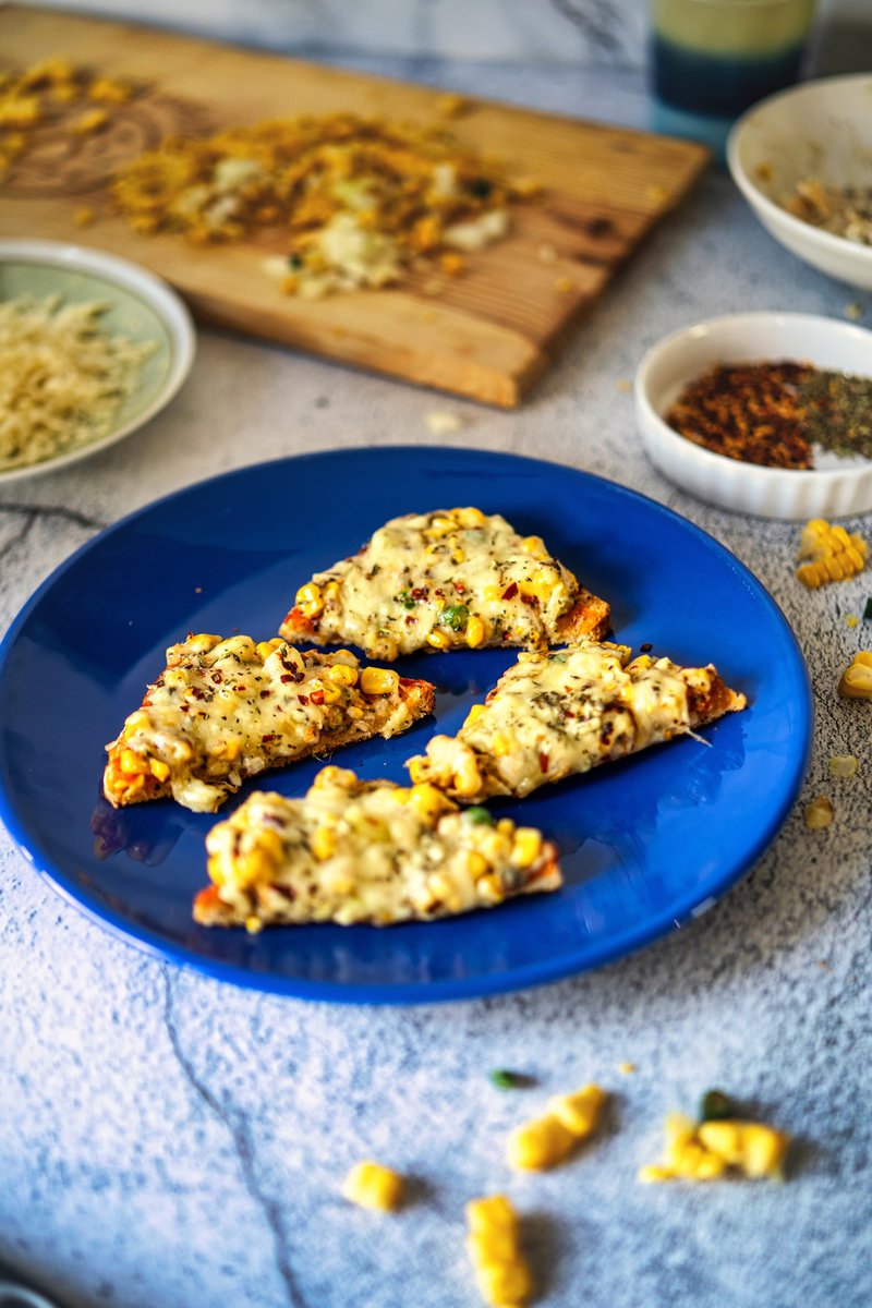 A close-up of Corn Chilli Cheese Toast served on a blue plate, showcasing the melted cheese and corn topping.