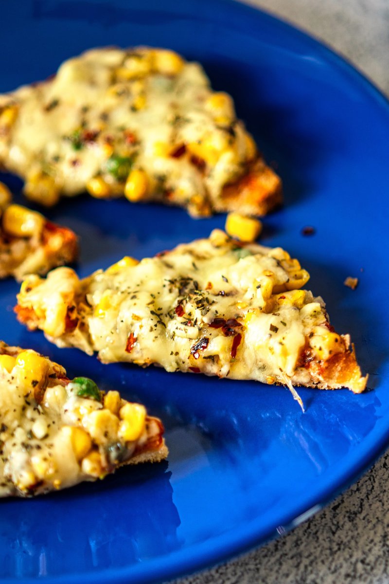 A zoomed-in view of Corn Chilli Cheese Toast on a blue plate, highlighting the texture and ingredients.