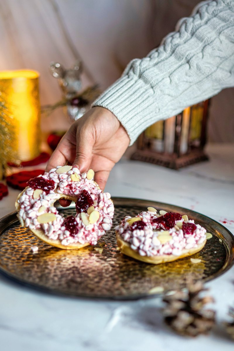  A hand reaching for a cottage cheese bagel topped with on a rustic metallic tray with candles in the background.