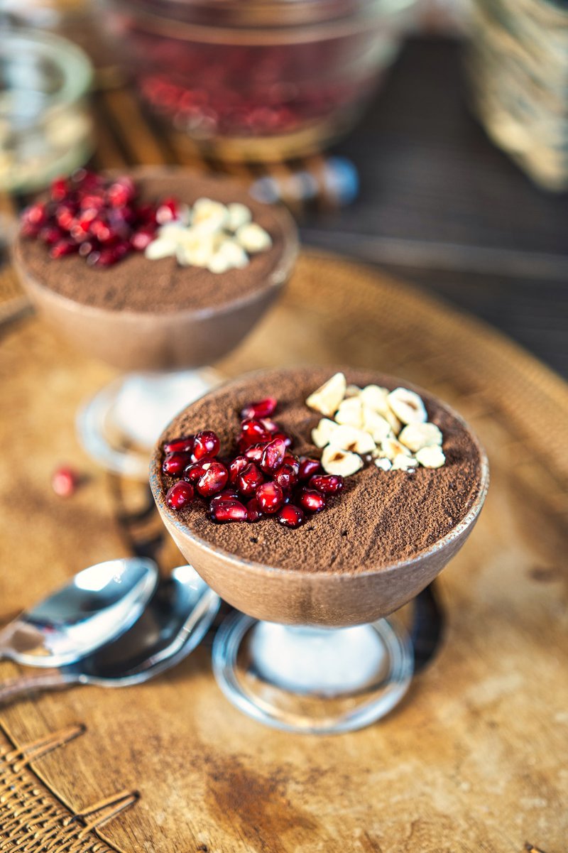 Two serving dishes of cottage cheese chocolate mousse garnished with pomegranate seeds and chopped nuts.