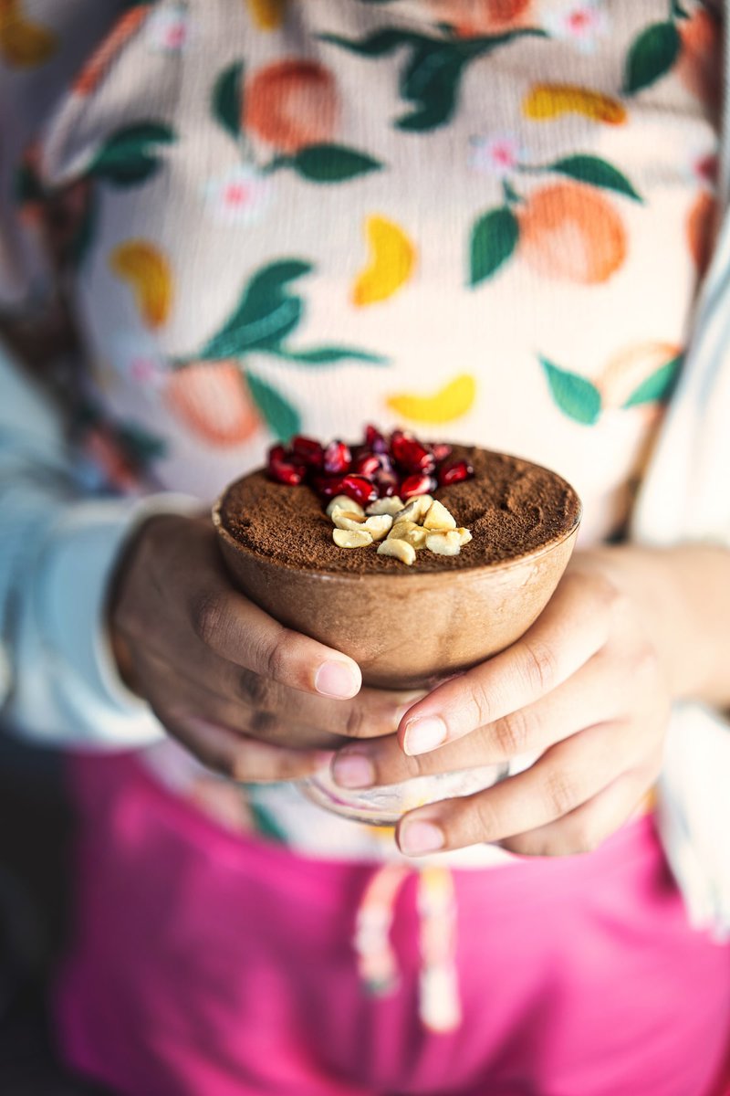 Person holding a bowl of high protien cottage cheese chocolate mousse topped with cocoa powder, pomegranate seeds, and nuts.