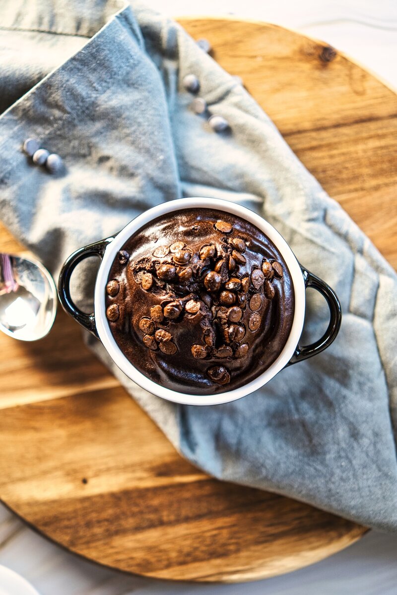 Cottage cheese chocolate mug cake with dark chocolate chips on top served on a wooden board, keto friendly high protein chocolate cake