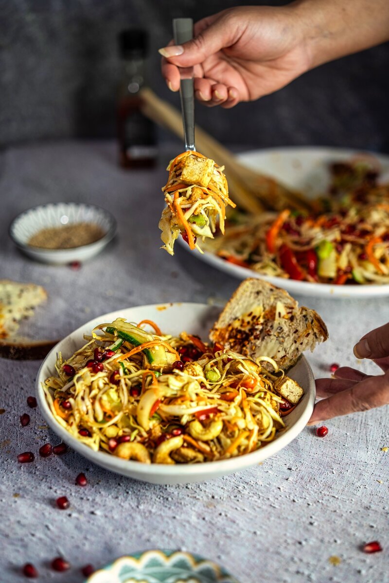 Close-up forkful of crunchy cabbage salad with roasted tofu, cashews, cucumber, and sesame ginger lime dressing