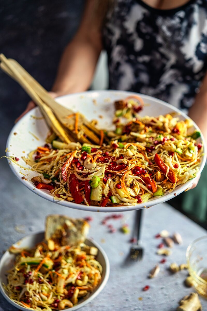 Crunchy sesame lime cabbage salad with tofu and cashews served in a large bowl with pomegranate and sesame ginger dressing
