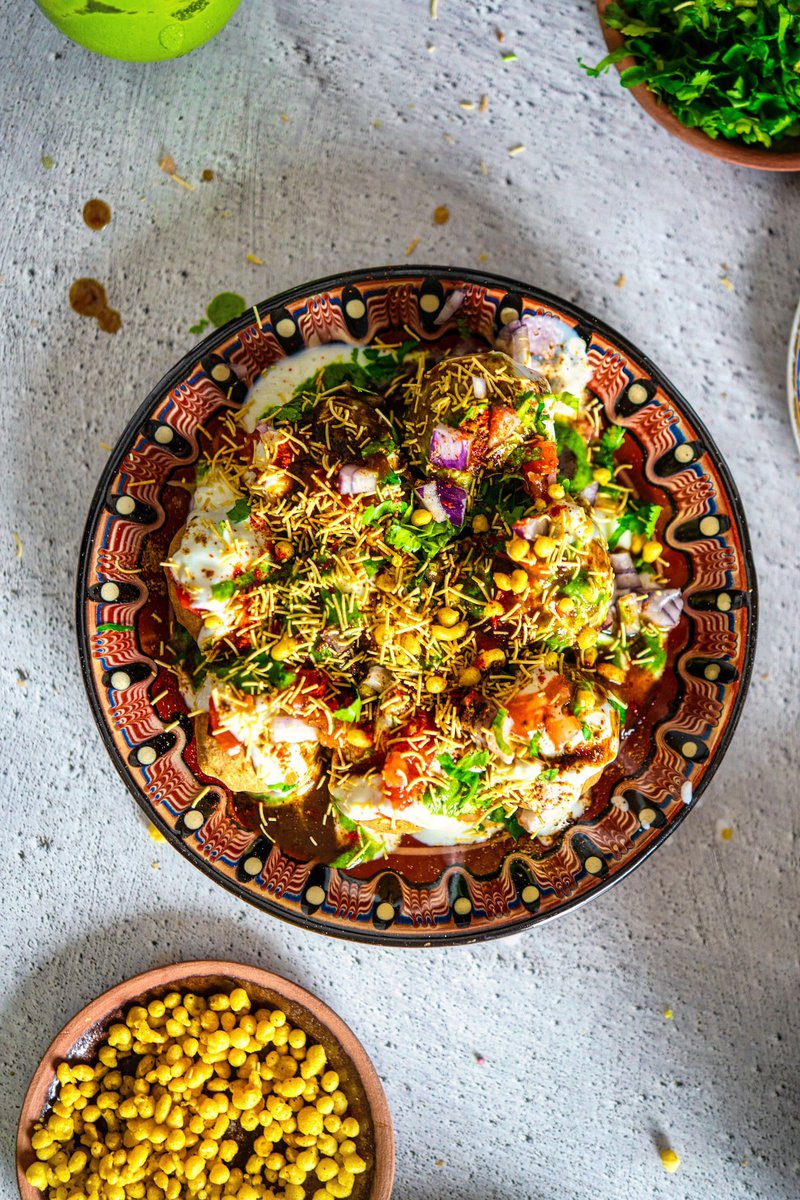 Overhead view of a plate filled with Dahi Puris, abundantly topped with yogurt, sev, onions, and chutneys on a patterned plate