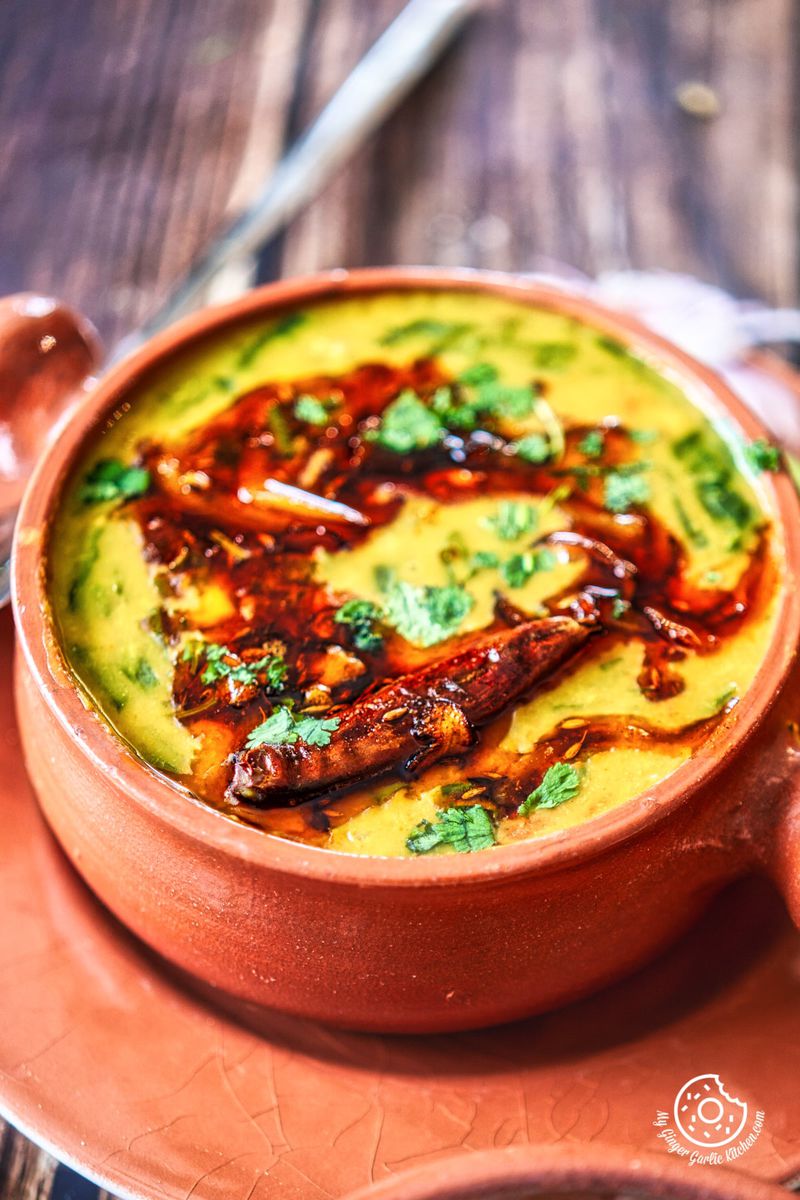close up shot of dal palak topped with tempering and cilantro served in a terra cotta bowl
