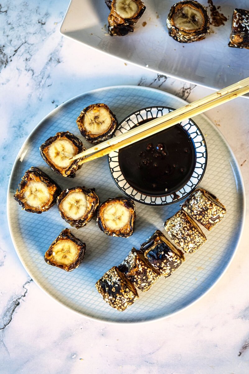 Overhead view of healthy date banana sushi slices with chocolate sauce and chopsticks