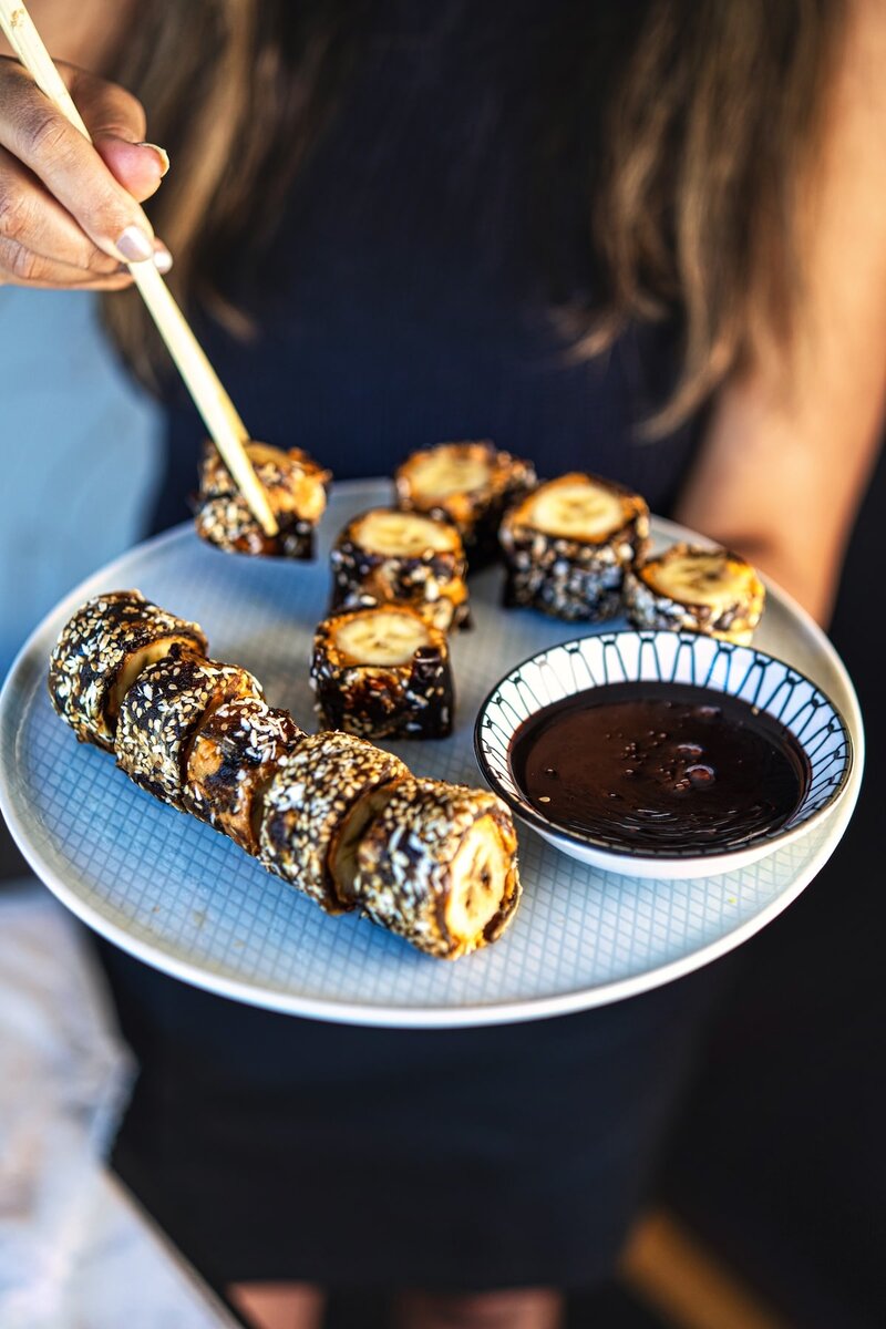 Banana peanut butter sushi rolls with dates served on plate with chocolate dipping sauce