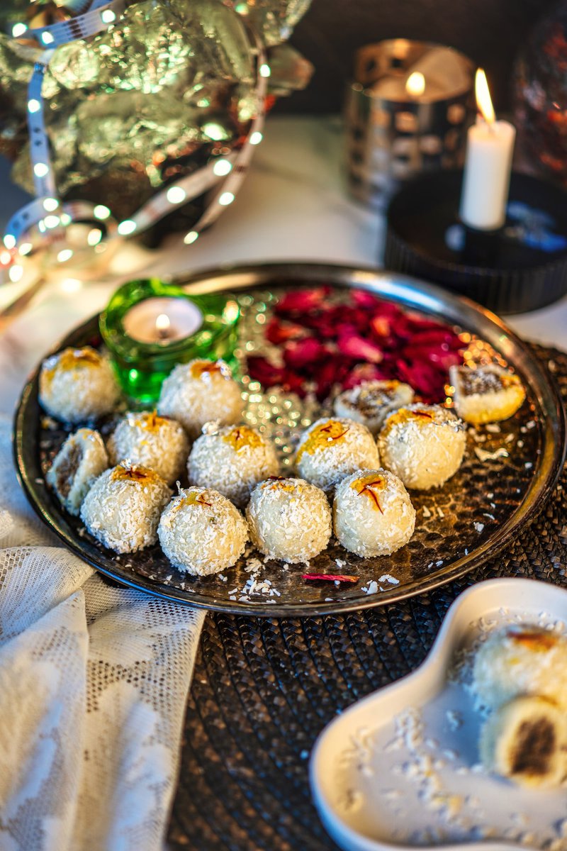 A beautifully arranged tray of date-stuffed coconut ladoos, garnished with saffron and surrounded by festive decor.