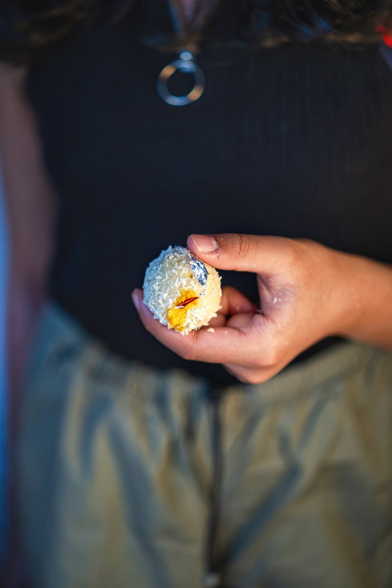 Hand holding a coconut ladoo stuffed with dates.