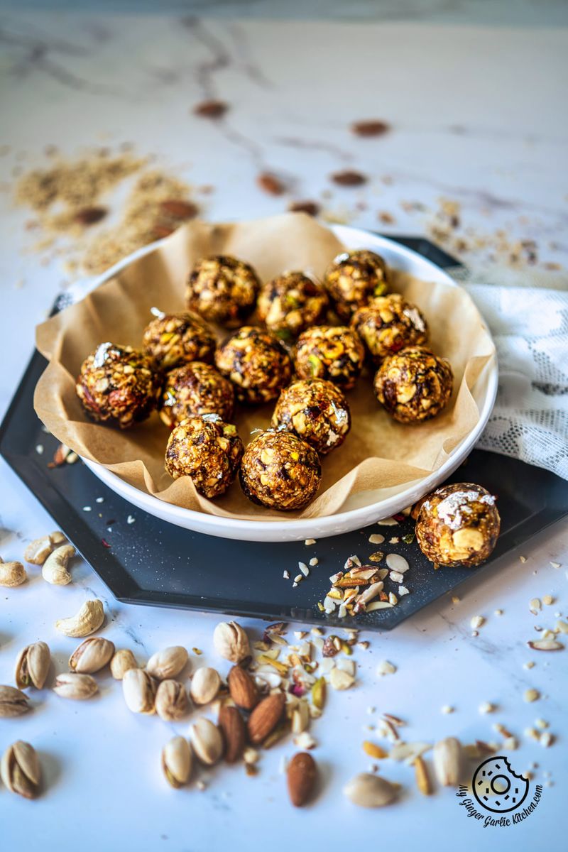 dry fruits laddu placed on a parchment paper line white plate and some nuts on the side