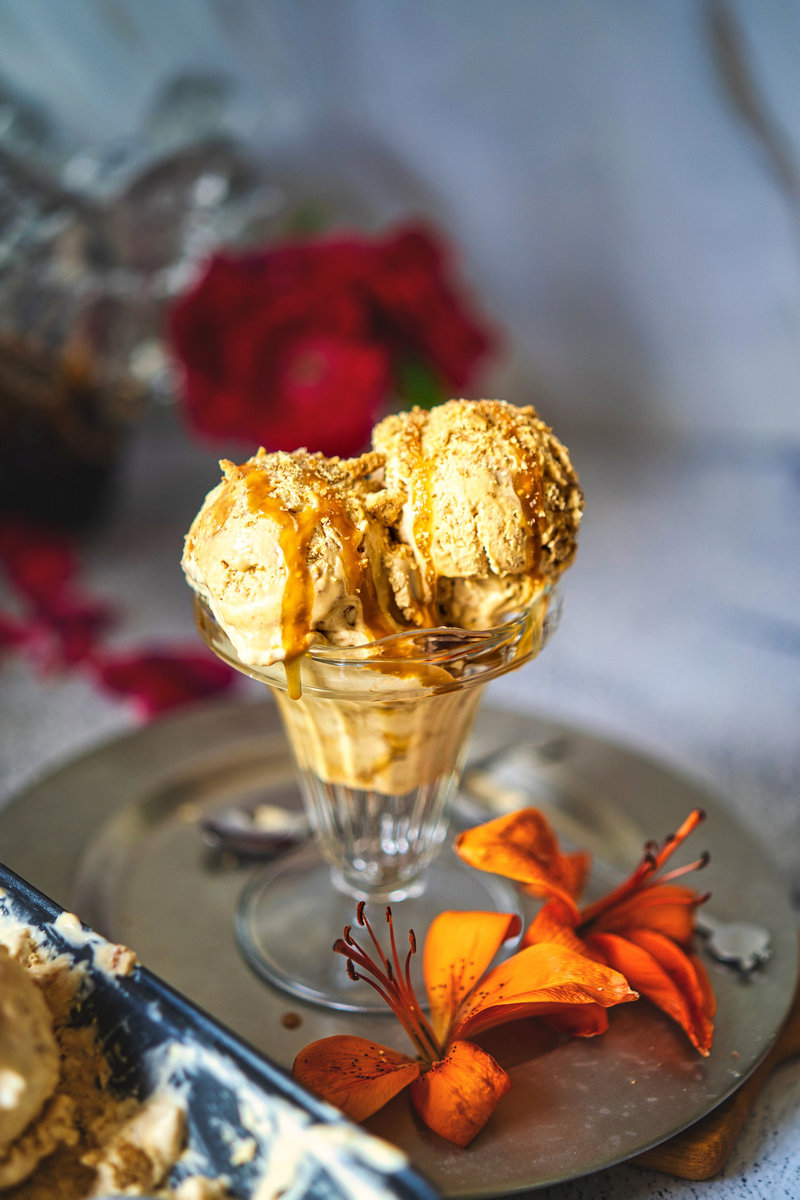 Glass dish with dulce de leche ice cream, caramel drizzle, and cookie crumbles on a silver tray with flowers