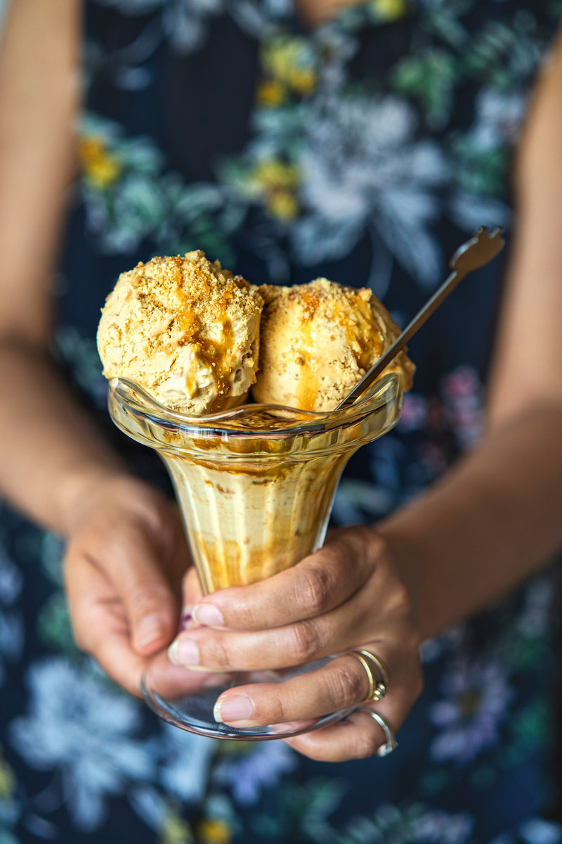 Person holding a glass dish of dulce de leche ice cream topped with caramel and cookies