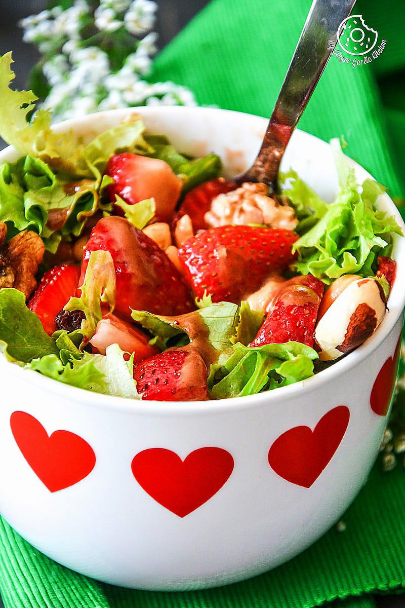 there is a bowl of salad with strawberries and nuts in it