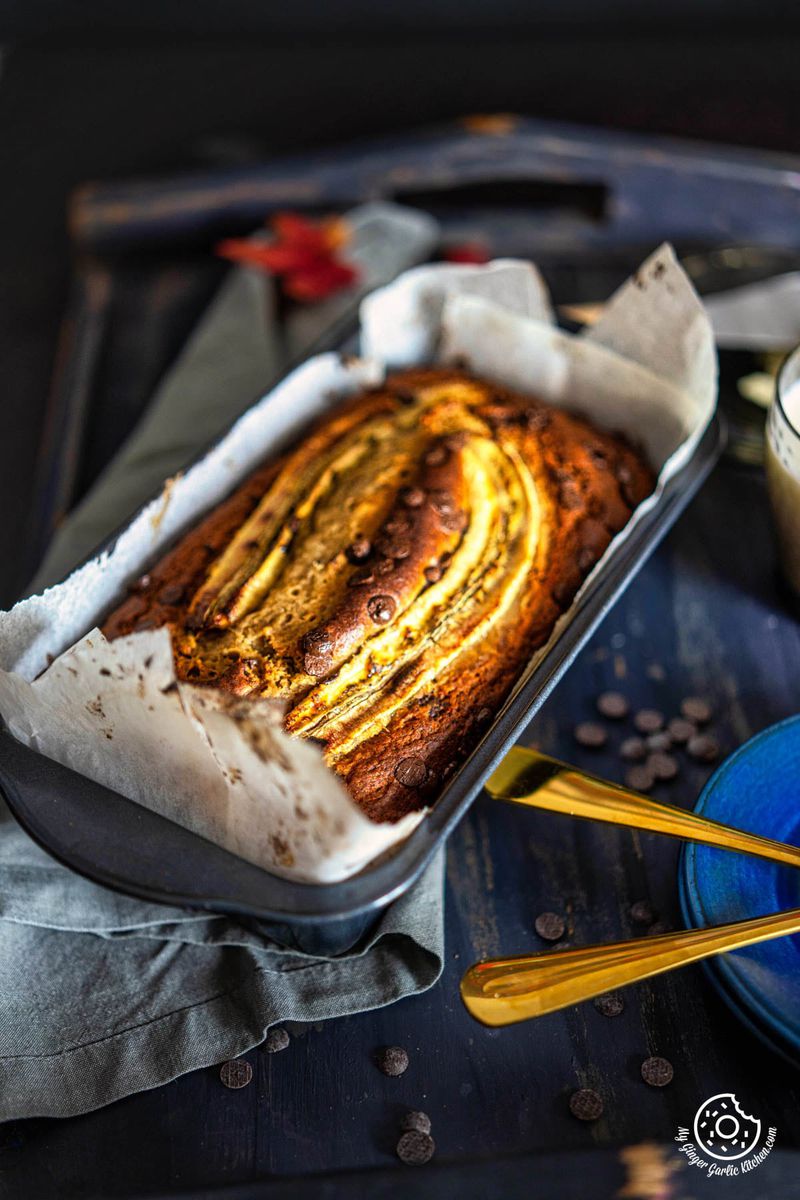 an eggless banana bread in a pan on a tray with a cup of coffee next to it