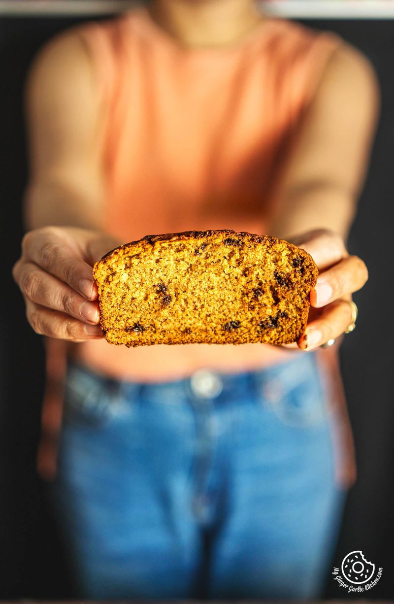 a woman holding up a slice of eggless banana bread