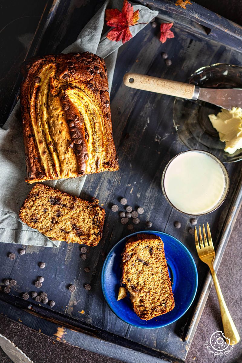 chocolate chip eggless banana bread on a blue tray with a knife and fork next to it