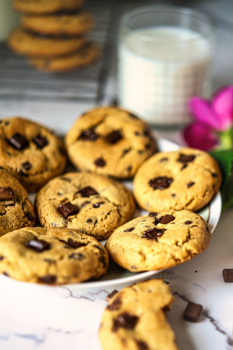 Plate of eggless chocolate chip cookies next to a glass of milk and a pink flower.