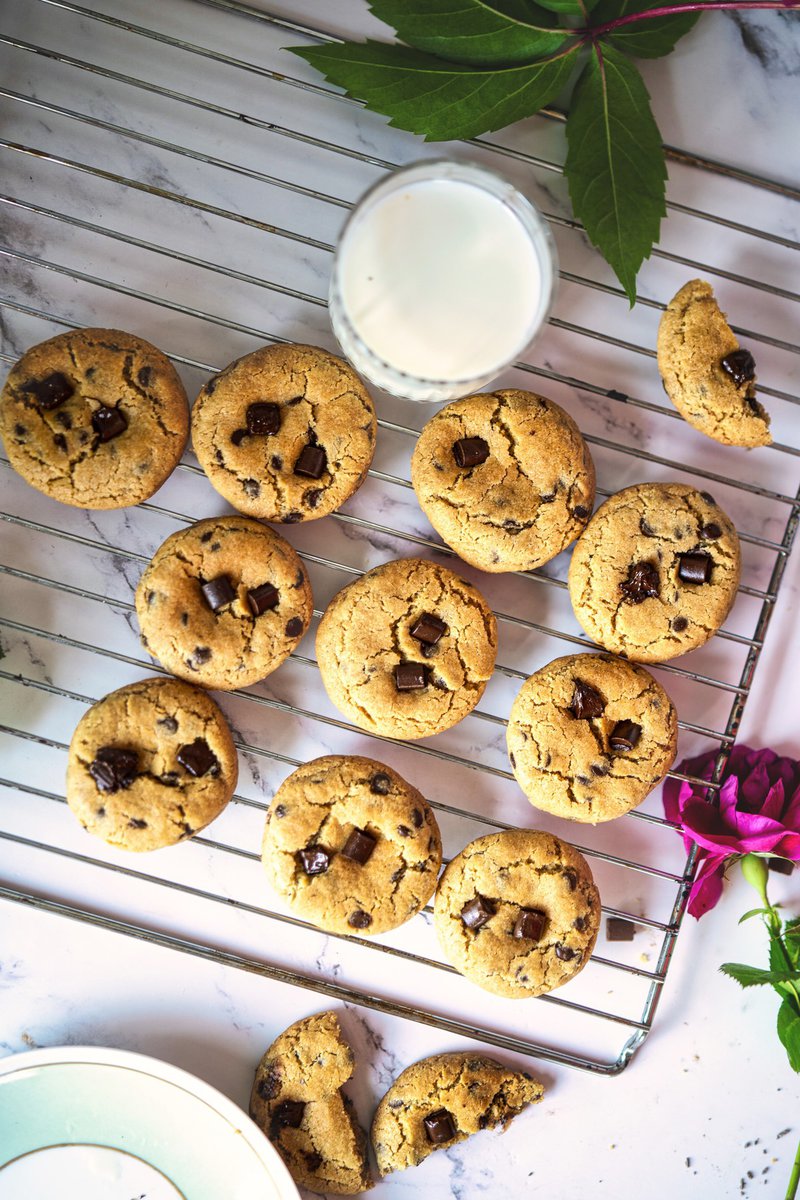 Freshly baked eggless chocolate chip cookies cooling on a wire rack with a glass of milk nearby.