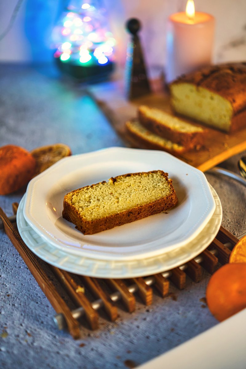 Eggless orange cake sliced and served on a plate, with a wooden board and other decorations in the background.