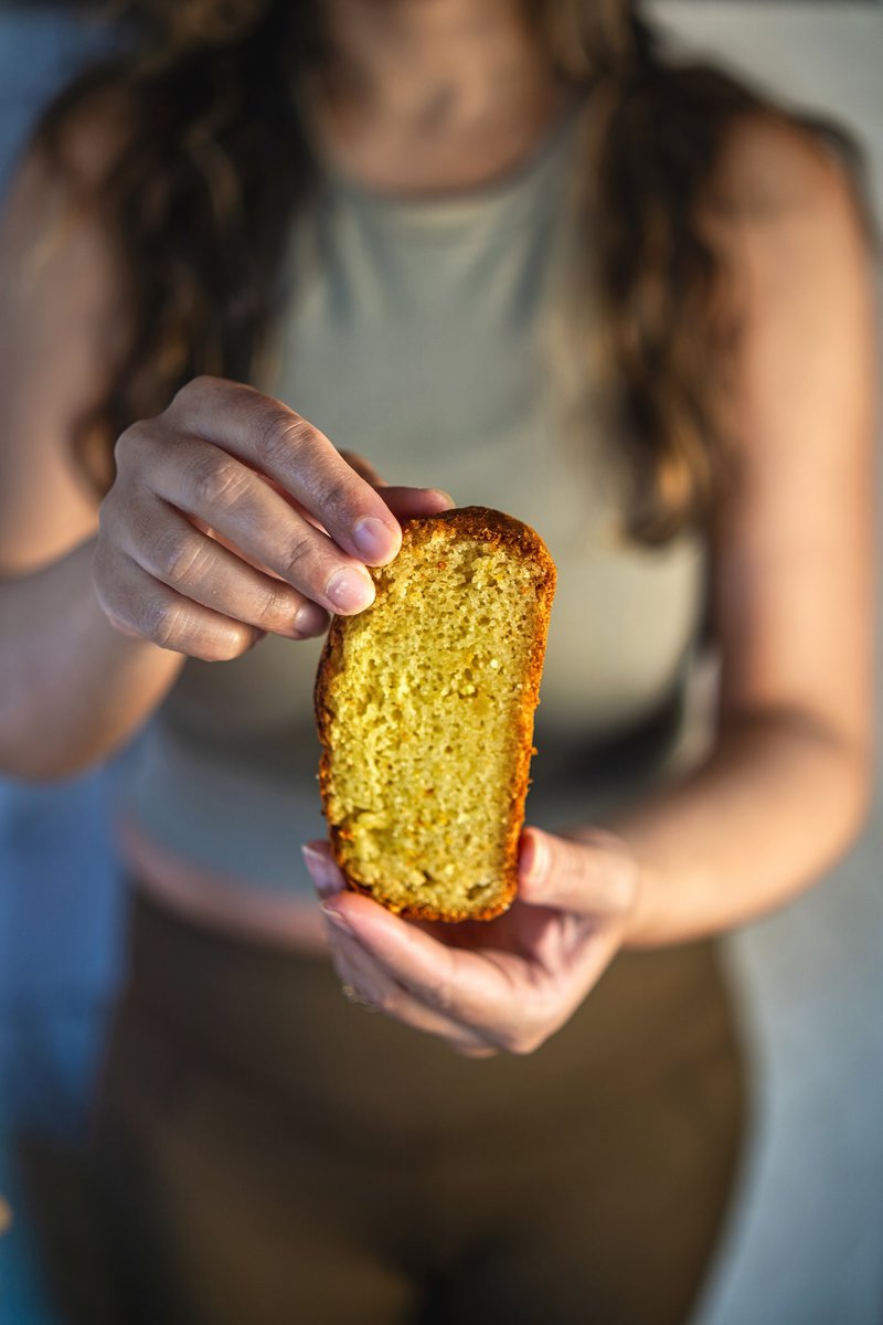 A person's hands holding a slice of eggless orange cake.