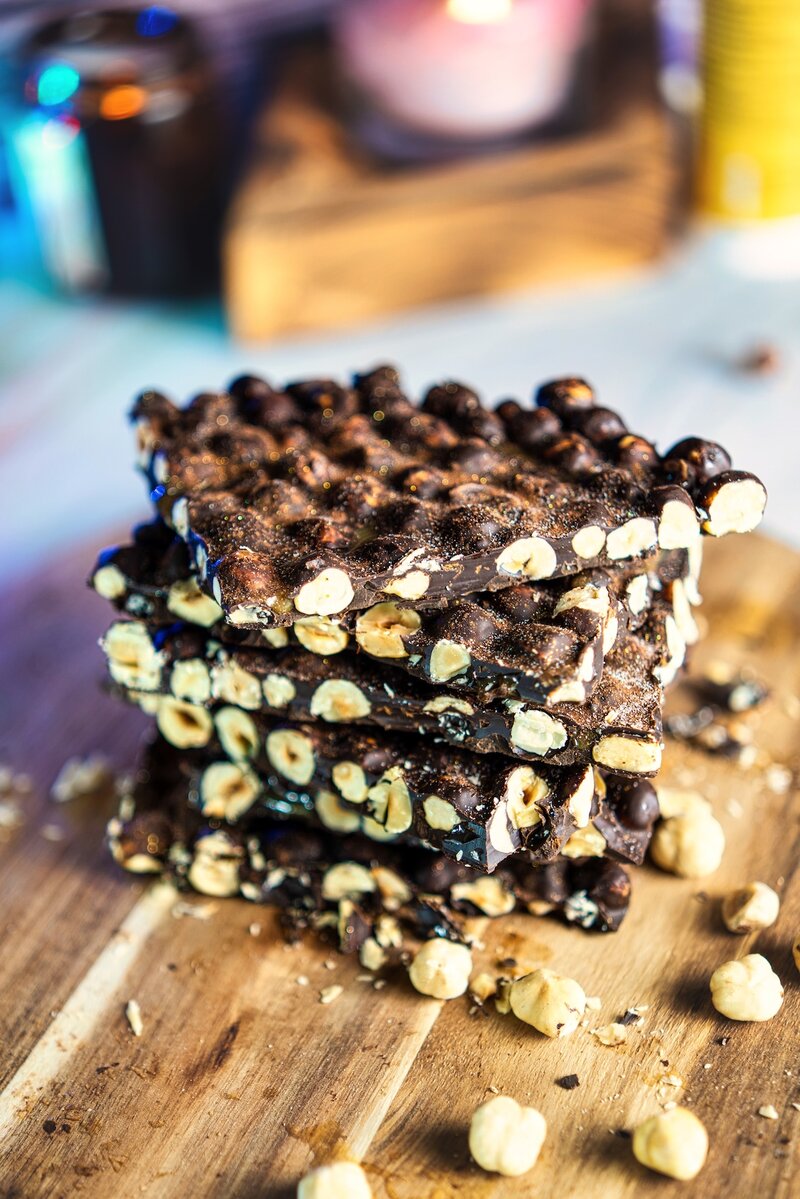 Stacked pieces of espresso hazelnut dark chocolate bark on wooden board, homemade chocolate bark with roasted hazelnuts