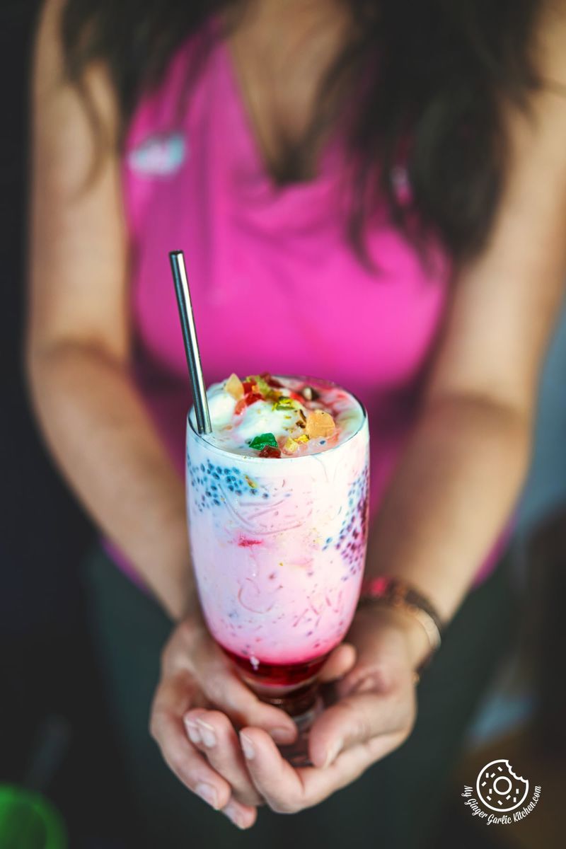 photo of a woman holding a glass of a colorful pink drink falooda