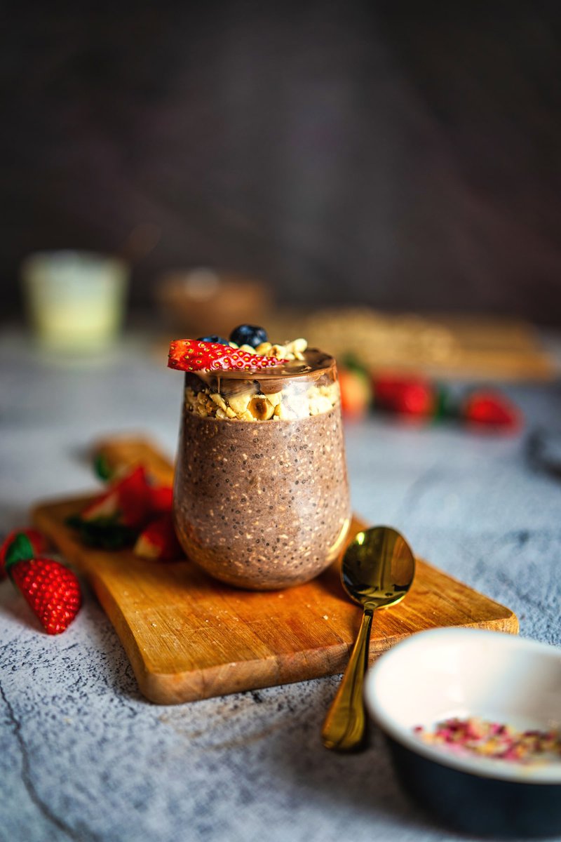 Gourmet Ferrero Rocher overnight oats served in a glass jar topped with strawberries and blueberries on a wooden cutting board.