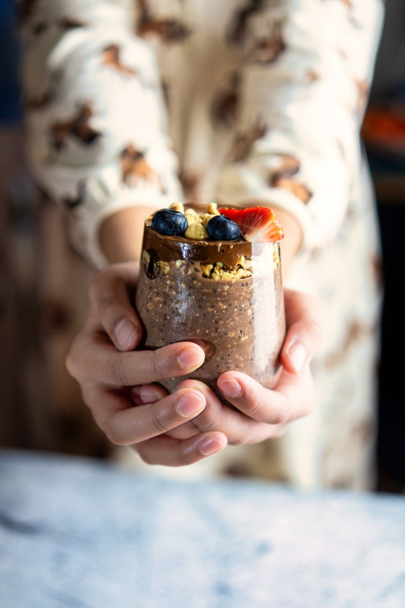 Woman holding a jar of Ferrero Rocher overnight oats topped with fresh berries and nuts, ready to be enjoyed.