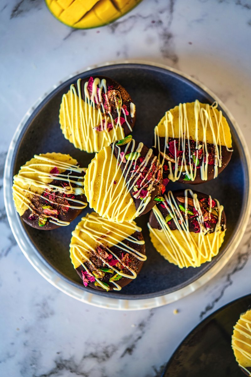 Frozen mango lassi bites dipped in dark chocolate and topped with pistachios and rose petals