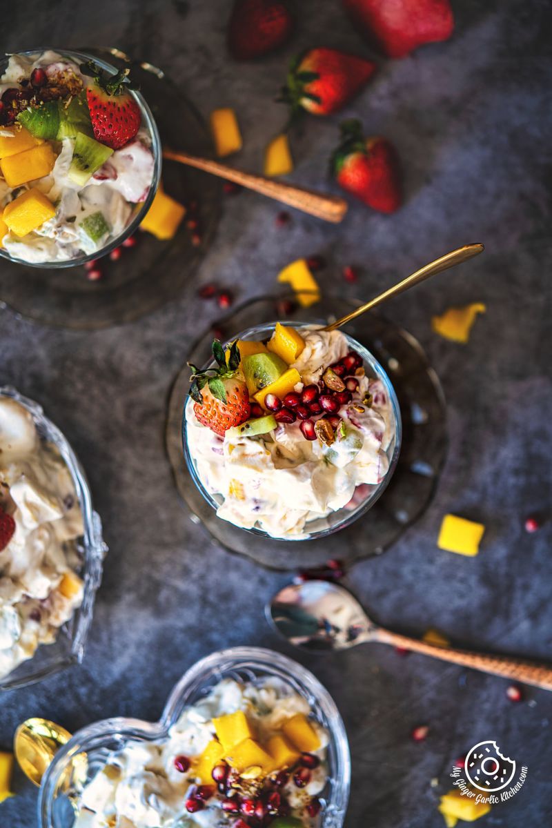 overhead view of fruit cream salad with 3 more bowls and fruits on the side