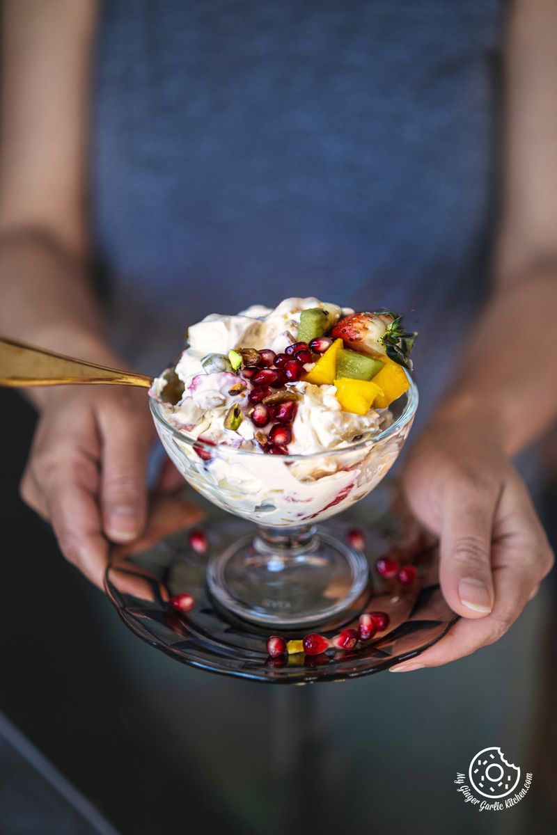 a female holding a fruit cream dessert topped with pomegranate in a transparent glass