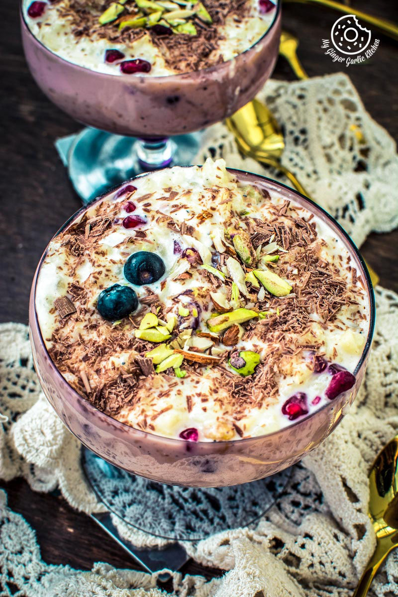 two fruit cream rice kheer indian pudding topped witn chocolate, and nuts in glasses on a table with a doily
