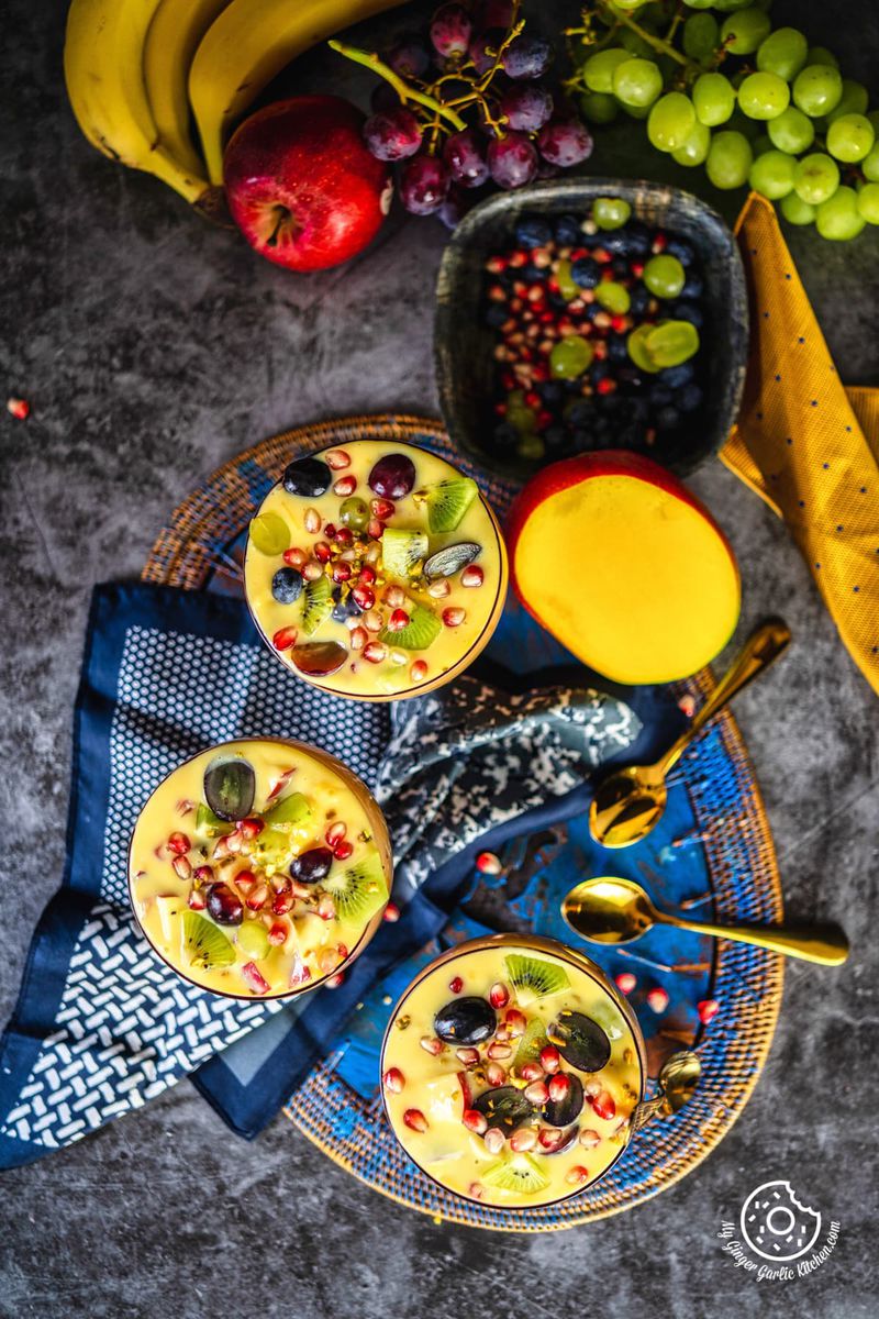 overhead shot of 3 fruit custard bowls with a half cut mango and other fruits